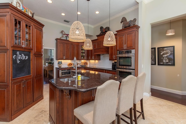 kitchen with double oven, decorative light fixtures, tasteful backsplash, an island with sink, and sink