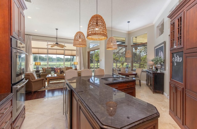 kitchen with sink, double oven, ornamental molding, a center island with sink, and decorative light fixtures