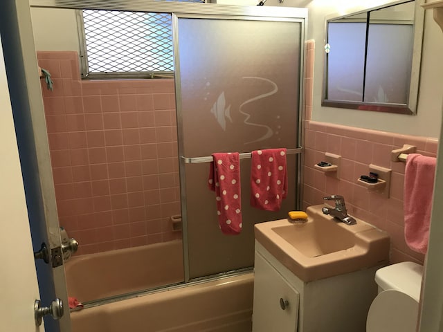 full bathroom featuring shower / bath combination with glass door, sink, tile walls, and toilet