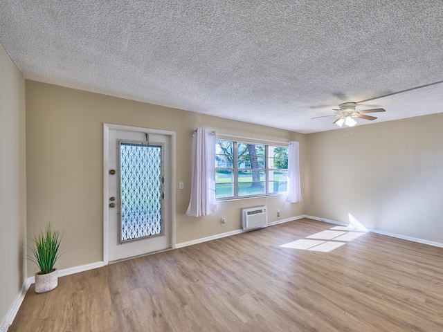 interior space with ceiling fan, light wood-type flooring, an AC wall unit, and a textured ceiling