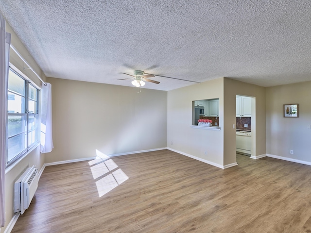 unfurnished room with ceiling fan, light hardwood / wood-style flooring, a textured ceiling, and radiator heating unit