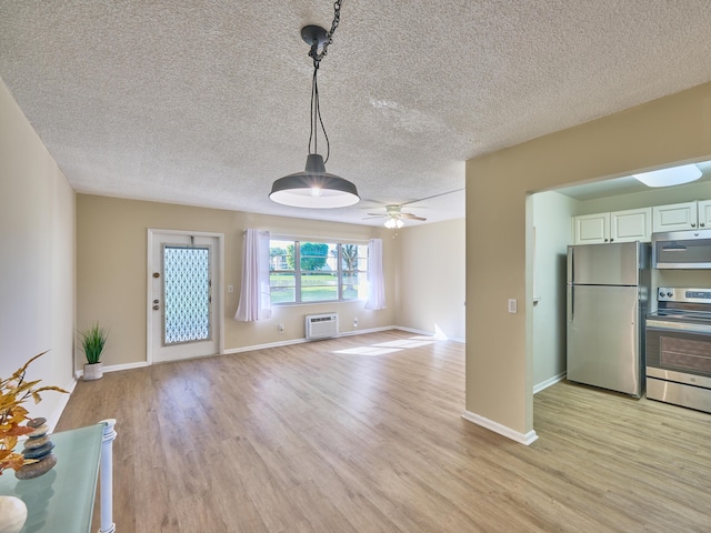 unfurnished living room with a wall mounted air conditioner, ceiling fan, a textured ceiling, and light hardwood / wood-style flooring