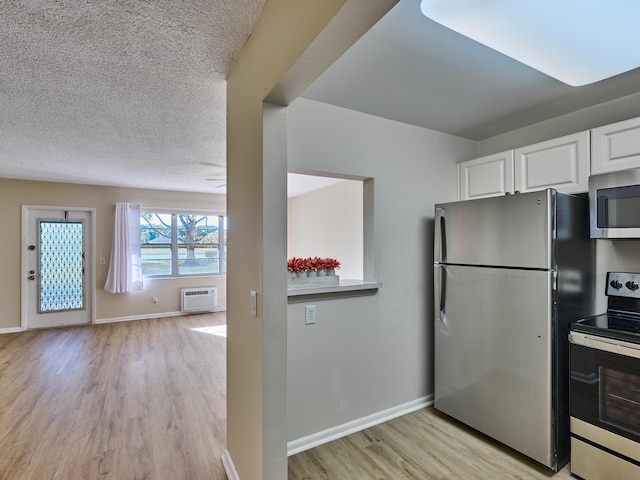 kitchen with a wall unit AC, white cabinetry, light hardwood / wood-style flooring, and stainless steel appliances