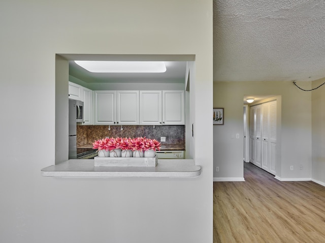 kitchen featuring backsplash, light wood-type flooring, a textured ceiling, white cabinetry, and stainless steel appliances