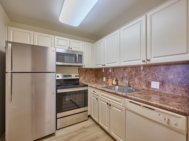 kitchen with appliances with stainless steel finishes, backsplash, sink, light hardwood / wood-style flooring, and white cabinets