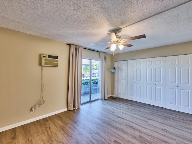 unfurnished bedroom with ceiling fan, a wall mounted air conditioner, hardwood / wood-style floors, a textured ceiling, and access to outside