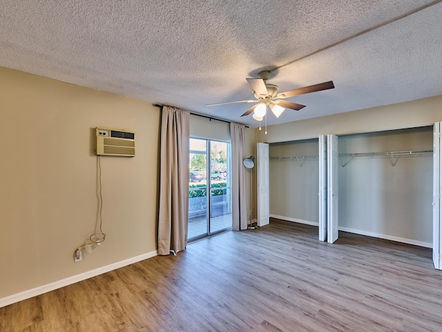 unfurnished bedroom featuring ceiling fan, light wood-type flooring, a textured ceiling, a wall mounted AC, and multiple closets