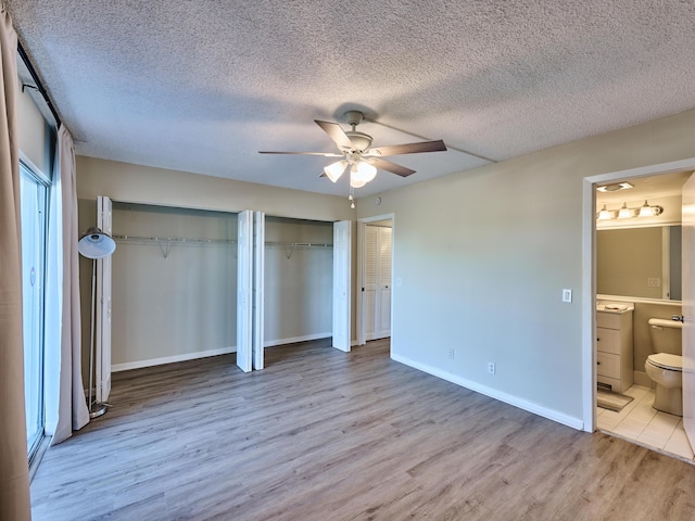 unfurnished bedroom featuring two closets, ensuite bathroom, ceiling fan, a textured ceiling, and light hardwood / wood-style floors