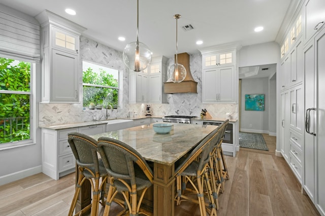 kitchen featuring custom range hood, a sink, backsplash, a breakfast bar area, and light wood finished floors