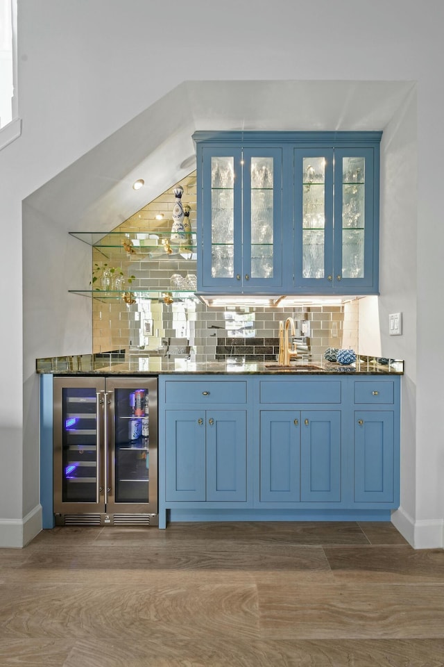 bar featuring blue cabinets, beverage cooler, sink, and decorative backsplash