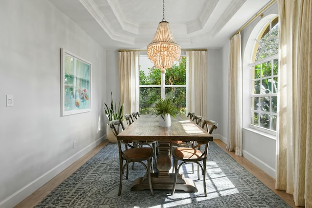 dining room featuring wood-type flooring, an inviting chandelier, a raised ceiling, and ornamental molding