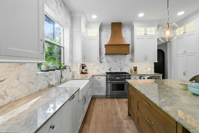 kitchen with premium range hood, decorative light fixtures, high end stove, sink, and white cabinets