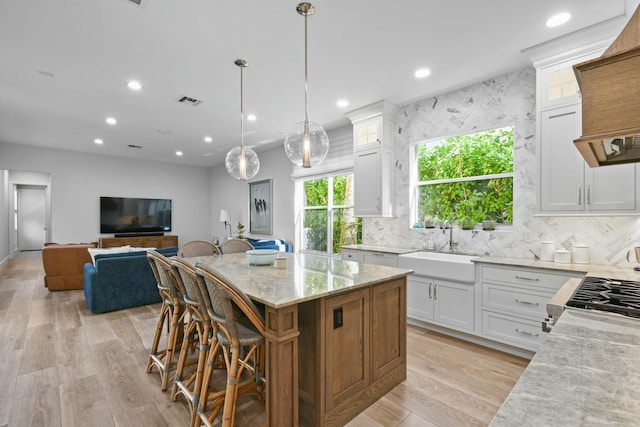 kitchen with a center island, pendant lighting, white cabinets, and light stone counters