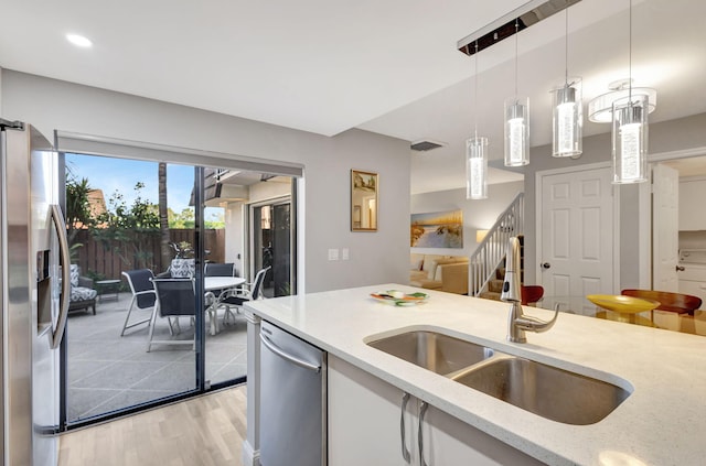 kitchen with appliances with stainless steel finishes, light stone counters, sink, decorative light fixtures, and light hardwood / wood-style flooring