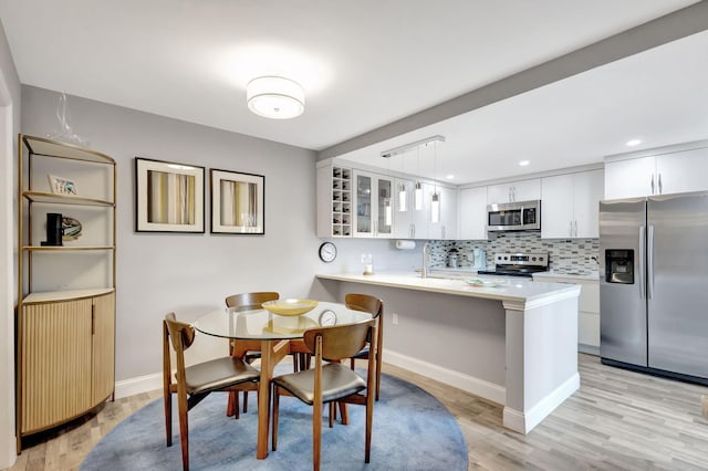 kitchen with kitchen peninsula, appliances with stainless steel finishes, a breakfast bar, pendant lighting, and white cabinetry