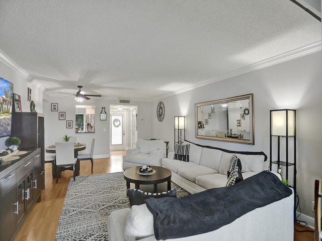 living room featuring ceiling fan, light hardwood / wood-style floors, ornamental molding, and a textured ceiling