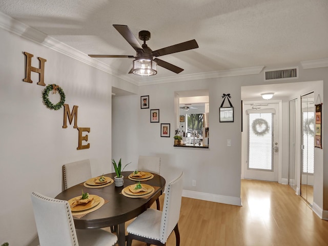 dining area with ceiling fan, light hardwood / wood-style floors, a textured ceiling, and ornamental molding