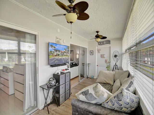 living room featuring ceiling fan, ornamental molding, a textured ceiling, and light hardwood / wood-style flooring