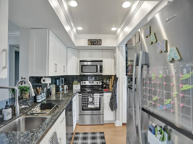 kitchen with sink, dark stone countertops, appliances with stainless steel finishes, white cabinets, and light wood-type flooring