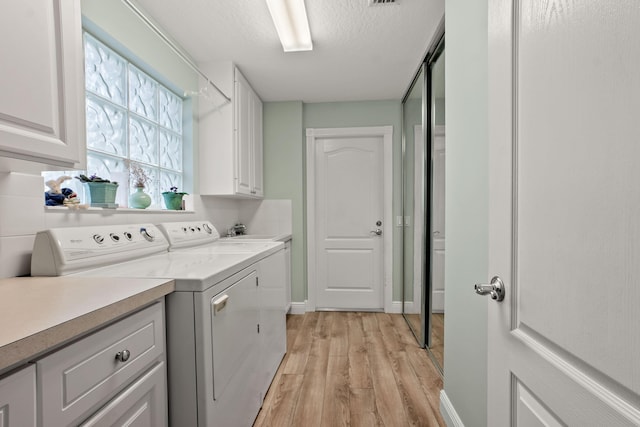 clothes washing area featuring cabinets, a textured ceiling, washing machine and dryer, and light hardwood / wood-style flooring