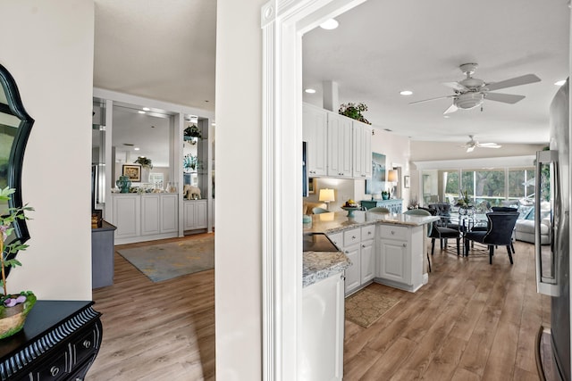 kitchen featuring kitchen peninsula, light stone countertops, ceiling fan, light hardwood / wood-style flooring, and white cabinets