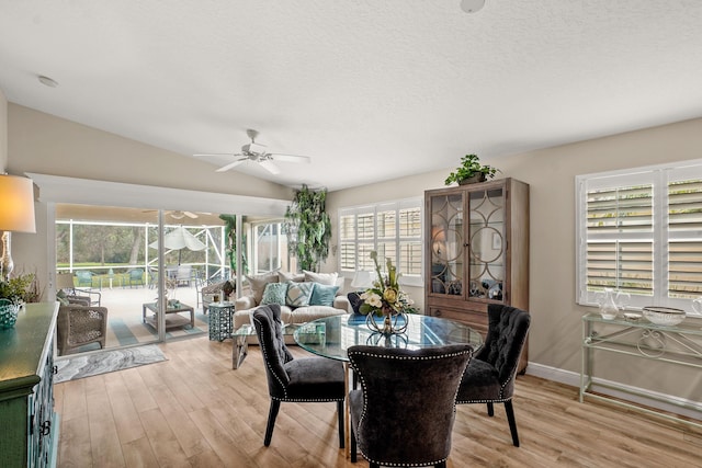 dining space featuring ceiling fan, lofted ceiling, a textured ceiling, and light hardwood / wood-style flooring