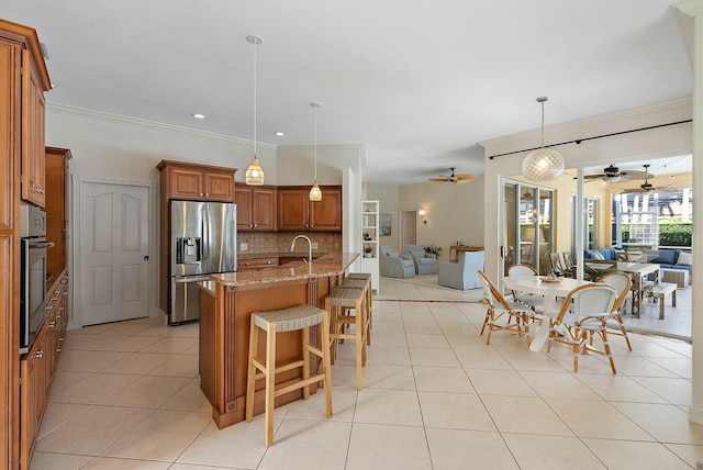 kitchen with hanging light fixtures, ornamental molding, tasteful backsplash, light stone counters, and stainless steel appliances