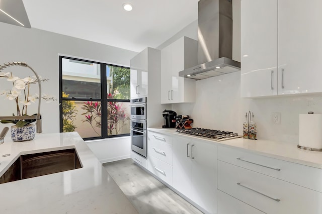 kitchen featuring sink, white cabinets, stainless steel appliances, and wall chimney range hood