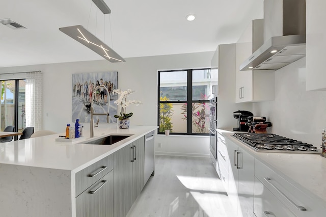 kitchen with sink, hanging light fixtures, wall chimney exhaust hood, a kitchen island, and stainless steel appliances