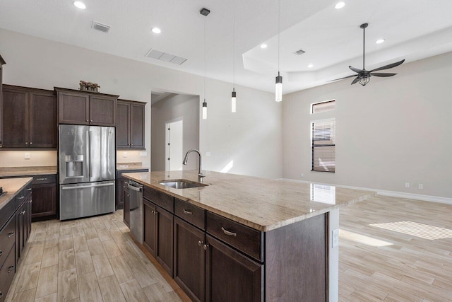 kitchen featuring ceiling fan, sink, stainless steel appliances, decorative light fixtures, and a kitchen island with sink