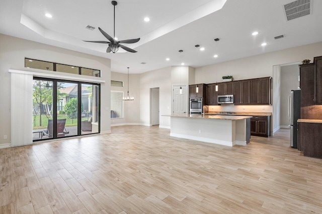 kitchen featuring a high ceiling, stainless steel appliances, a tray ceiling, and an island with sink