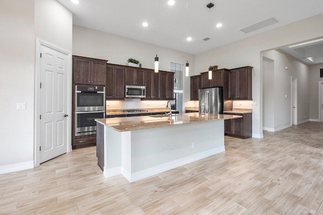 kitchen featuring sink, stainless steel appliances, light stone counters, pendant lighting, and a kitchen island with sink