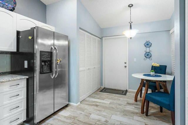 kitchen with white cabinetry, stainless steel fridge with ice dispenser, light stone counters, backsplash, and pendant lighting