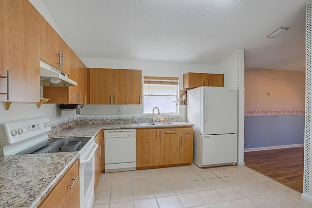 kitchen with a textured ceiling, light stone counters, white appliances, and sink