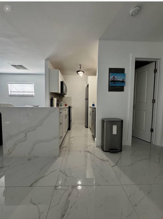 kitchen featuring white cabinets, stainless steel refrigerator, and light stone counters