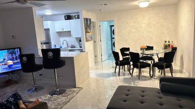 kitchen with stainless steel refrigerator, sink, stacked washer / dryer, a kitchen bar, and white cabinets