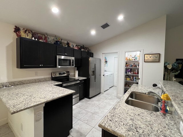 kitchen with appliances with stainless steel finishes, washer and dryer, lofted ceiling, sink, and light stone counters