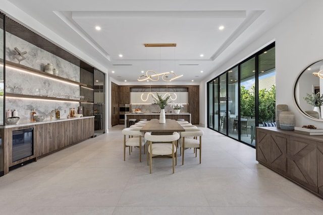 dining space featuring a chandelier, a wall of windows, wine cooler, and a tray ceiling