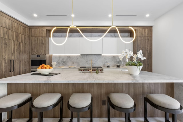 kitchen with stainless steel oven, sink, tasteful backsplash, a kitchen bar, and white cabinets