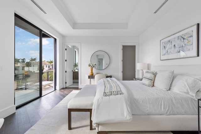 bedroom featuring connected bathroom, dark hardwood / wood-style flooring, access to outside, and a tray ceiling