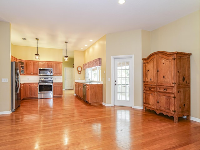 kitchen with pendant lighting, stainless steel appliances, light wood-type flooring, and sink