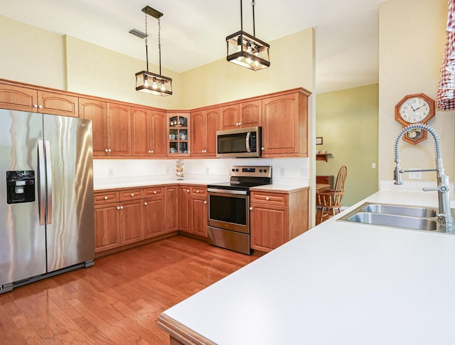 kitchen featuring backsplash, sink, hardwood / wood-style flooring, decorative light fixtures, and stainless steel appliances