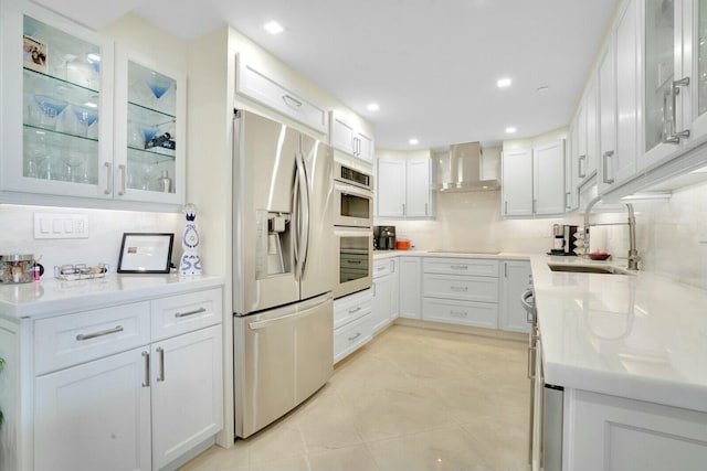 kitchen featuring sink, wall chimney range hood, decorative backsplash, white cabinets, and appliances with stainless steel finishes