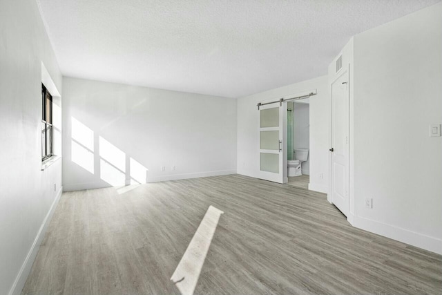 empty room with wood-type flooring, a barn door, and a textured ceiling