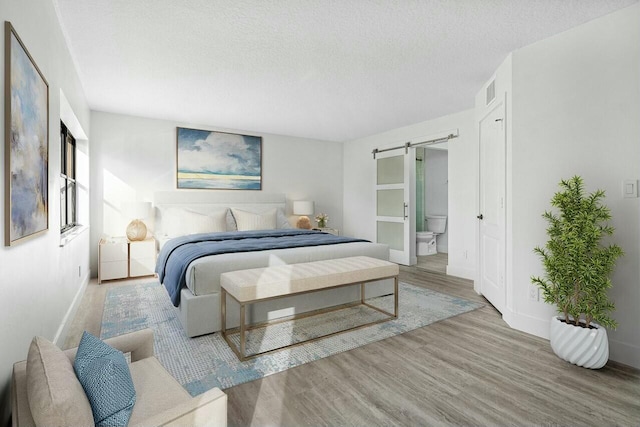 bedroom with a barn door, a textured ceiling, and light wood-type flooring