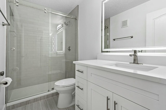 bathroom with vanity, toilet, an enclosed shower, and a textured ceiling