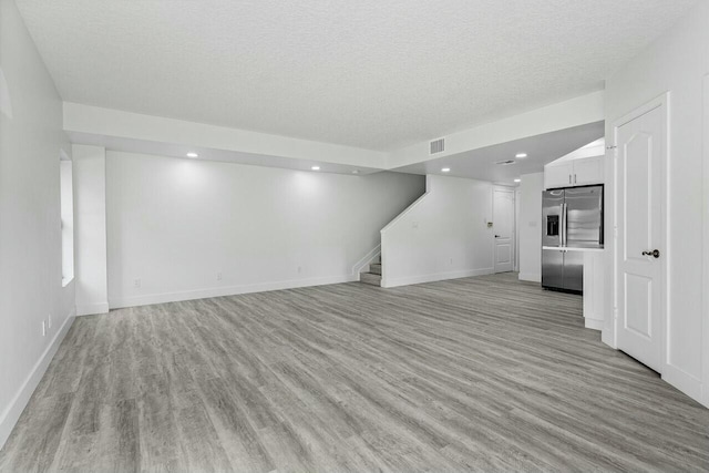 unfurnished living room with a textured ceiling and light hardwood / wood-style flooring