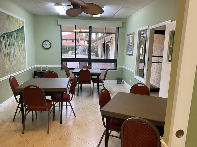 dining space featuring light tile patterned floors, baseboards, a drop ceiling, and ceiling fan