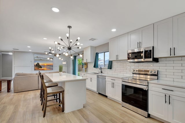 kitchen with a breakfast bar, stainless steel appliances, white cabinetry, a kitchen island, and hanging light fixtures