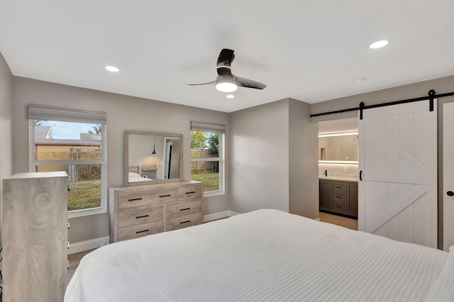 bedroom featuring ceiling fan, a barn door, ensuite bathroom, and light hardwood / wood-style flooring